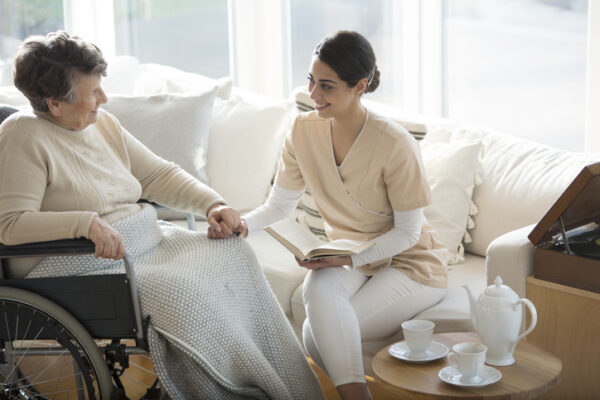 Elderly woman in wheelchair sitting with a caregiver in her sun room.