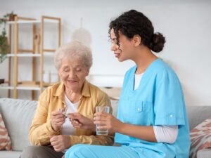 Caregiver helps elderly woman take medication at home while offering support and care